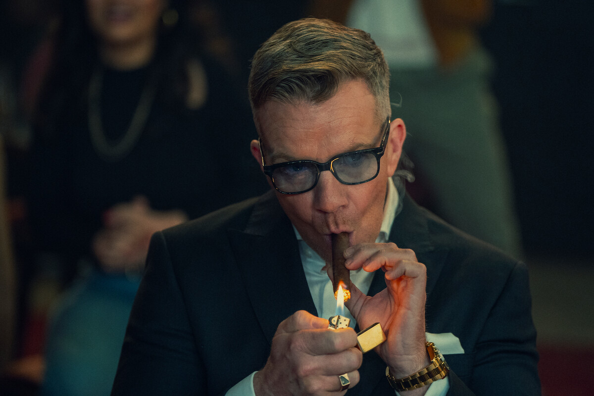 Henry Collins — Max Beesley as Henry Collins lights a cigar in season 1 of ‘The Gentlemen’