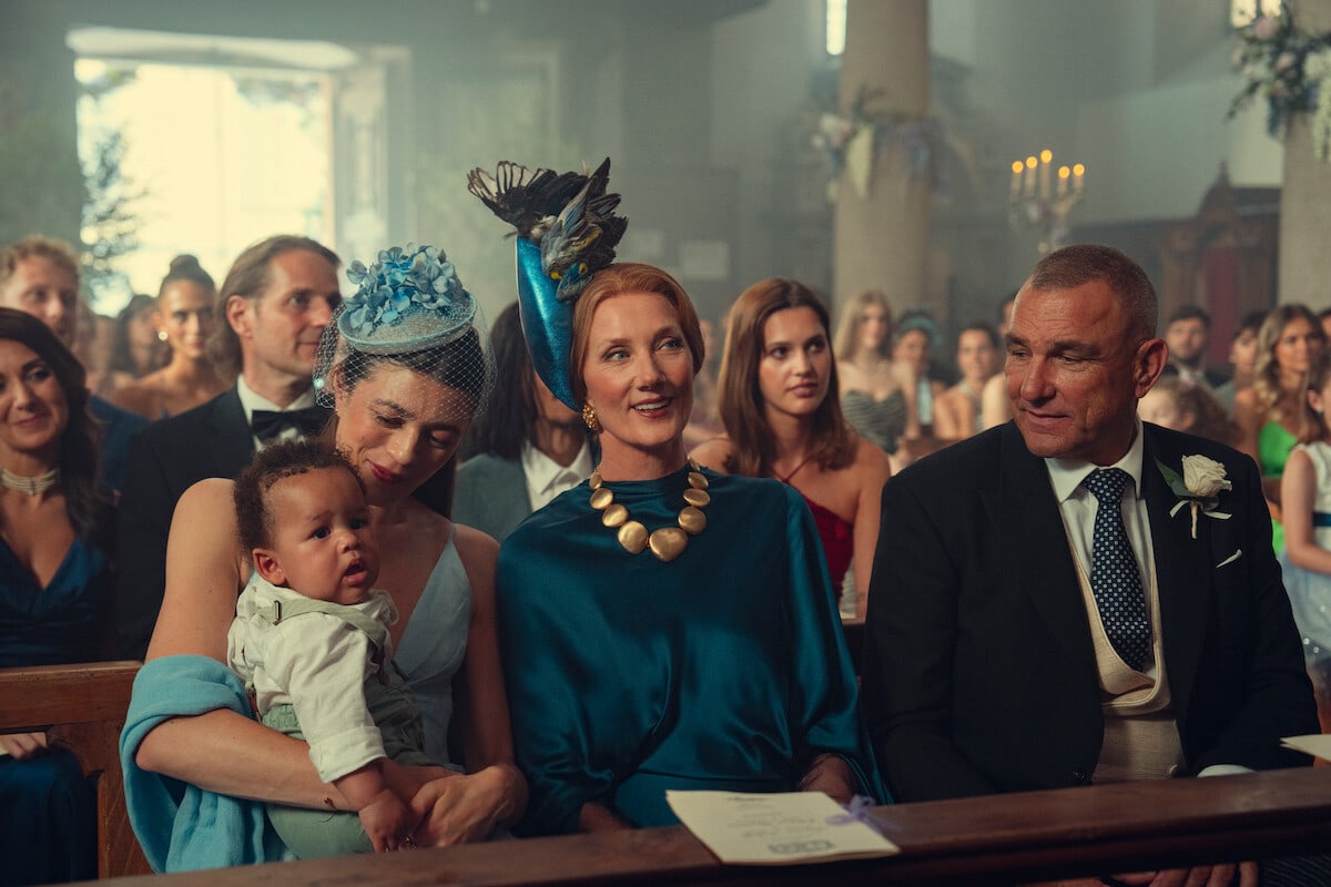 Tarquin — People dressed formally sitting in pews at a wedding ceremony inside a church, with women wearing hats and a woman holding a baby; candles and floral decorations are visible in the background.